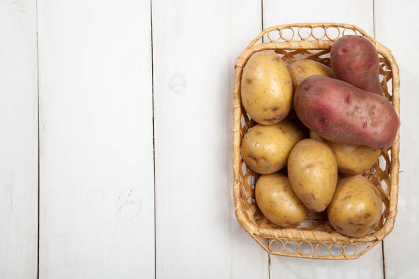 Raw potatoes with burlap on white wooden background, top view