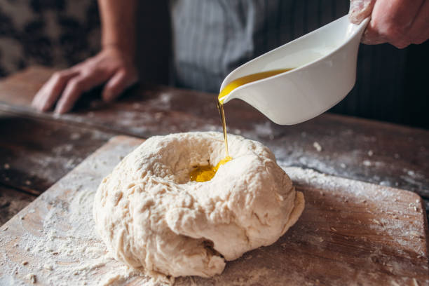 aggiunta di olio d'oliva al primo primo passo dell'impasto crudo - impastare foto e immagini stock