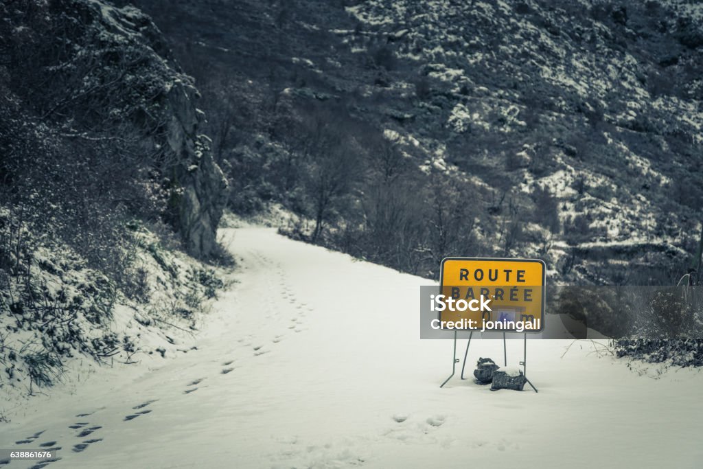 Road blocked sign on snow covered mountain road in Corsica Yellow road blocked sign at the start of a snow covered mountain road disappearing into the distance in the Balagne region of Corsica Block Shape Stock Photo