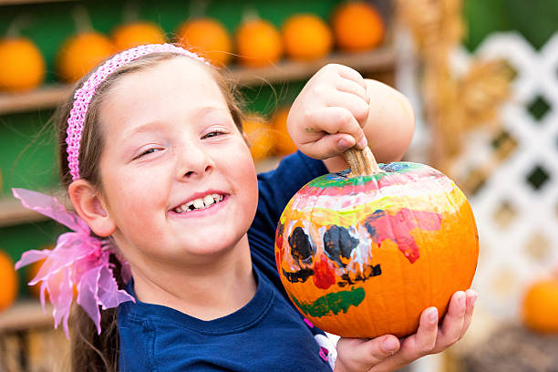 lächelndes kleines mädchen zeigt ihren bemalten kürbis - pumpkin child little girls pumpkin patch stock-fotos und bilder