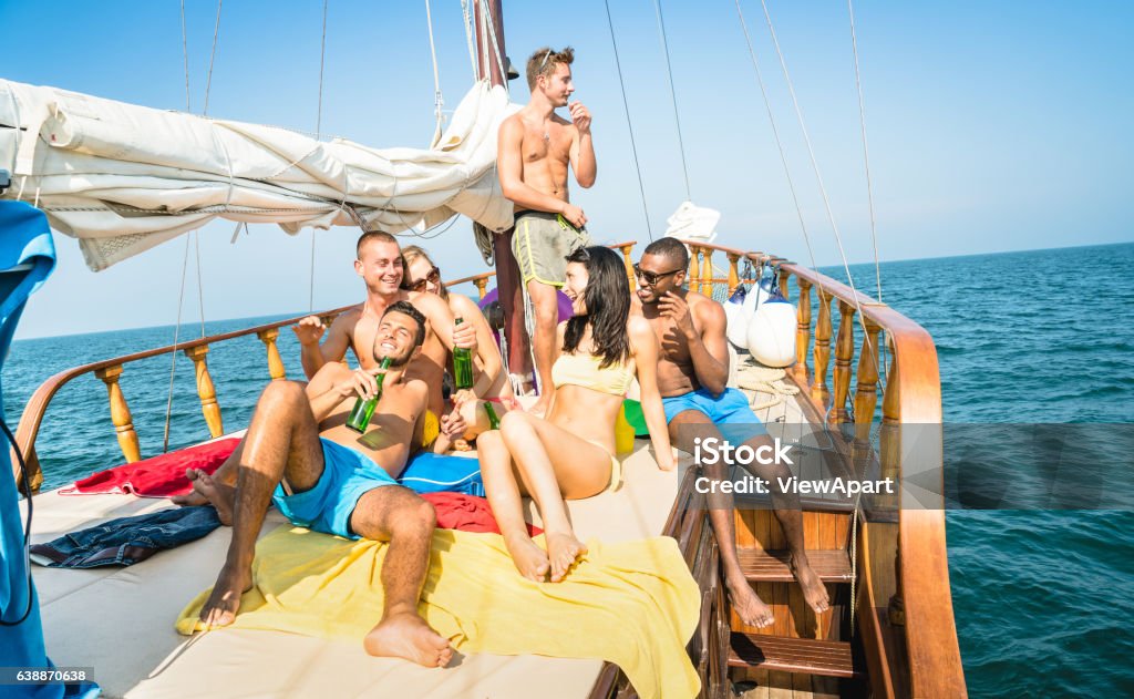 Felices amigos multirraciales bebiendo cerveza y divirtiéndose en velero - Foto de stock de Embarcación marina libre de derechos