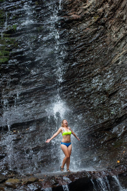 istock Girl in swimming suit standing under waterfall 638873500