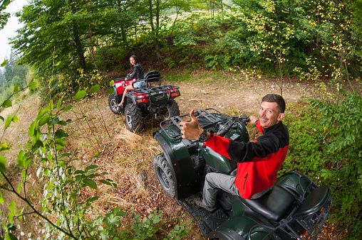 Happy beautiful couple driving four-wheelers ATV. Man looking to the camera and giving thumb up