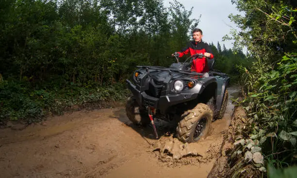 Young guy driving four-wheeler ATV through mud