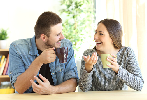 Front view of a casual couple talking looking each other during breakfast in a table of the living room at home