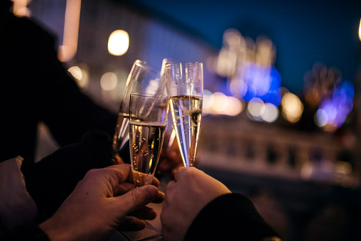 Three friends are toasting with champagne in the city at night. We can see christmas lights in back.