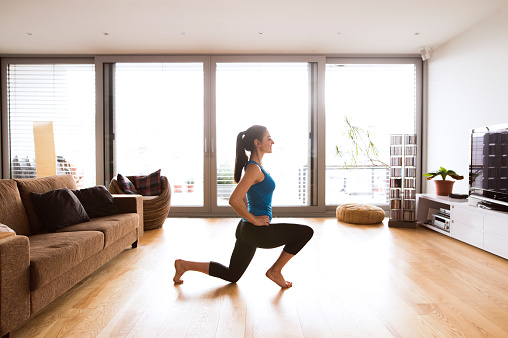 Beautiful young woman working out at home in living room, doing yoga or pilates exercise, stretching legs.