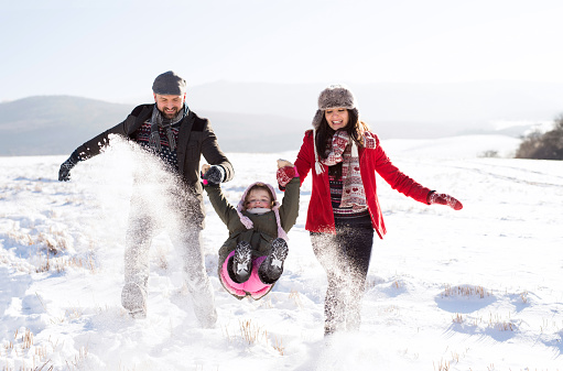 Father and mother having fun with their daughter, playing in the snow. Sunny white winter nature.