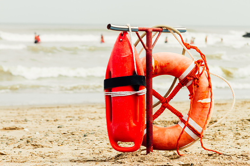 Ring buoy and can of lifeguard on the beach with sea with people in the background