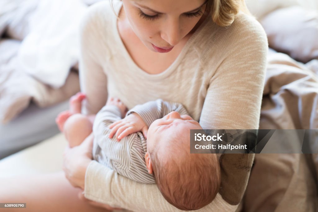 Beautiful young mother holding baby son in her arms Beautiful young mother holding her baby son in her arms Bed - Furniture Stock Photo