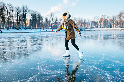Black skates on ice. Women's legs in burgundy pants stand on the surface of a frozen forest lake.