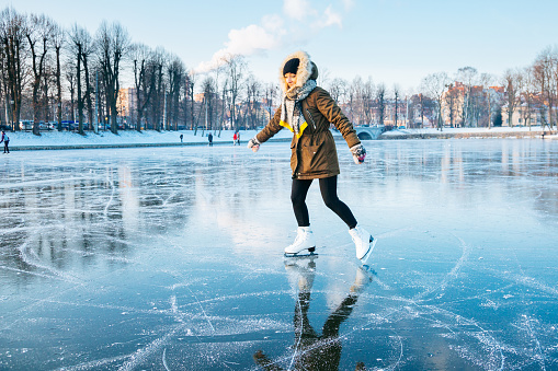 Ice skating on the frozen lake. Young woman on ice skates in sunset.