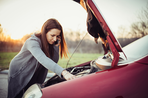 Woman on the road trying to fix the broken car, and calling for help on her mobile phone.