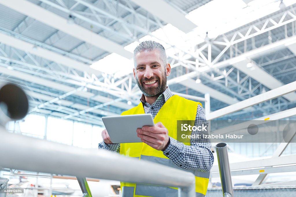 Aircraft engineer using a digital tablet in a hangar Aircraft engineer using a digital tablet in a hangar, smiling at camera, airplane in the background. Engineer Stock Photo