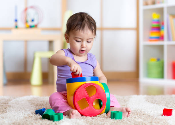 Cтоковое фото малыш девушка играет в помещении с сортер игрушка сидит на мягкой