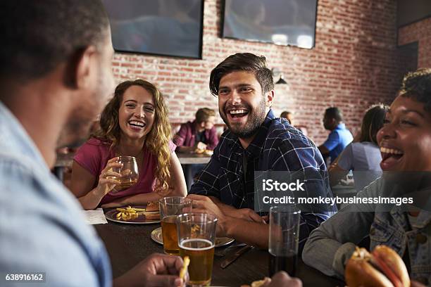 Friends Eating Out In Sports Bar With Screens In Background Stock Photo - Download Image Now