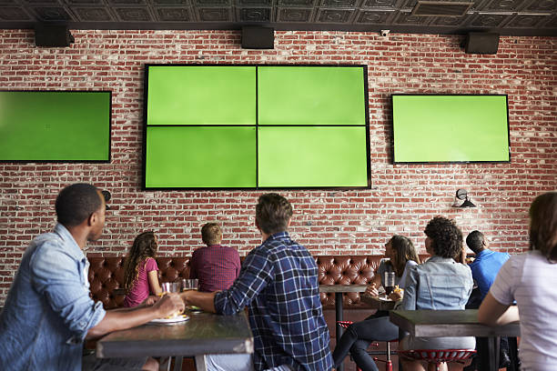 Rear View Of Friends Watching Game In Sports Bar On Rear View Of Friends Watching Game In Sports Bar On Screens bar counter stock pictures, royalty-free photos & images
