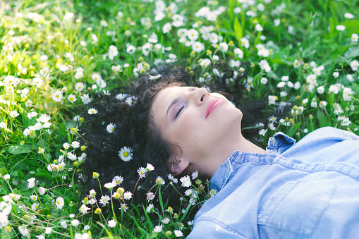 Beautiful young woman laying on a green grass with white flowers in a park.
