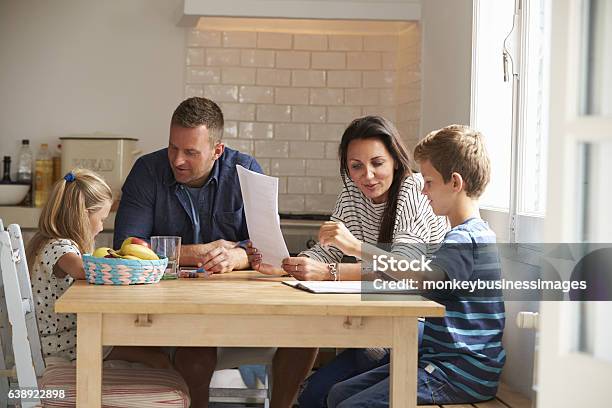 Parents Helping Children With Homework At Kitchen Table Stock Photo - Download Image Now