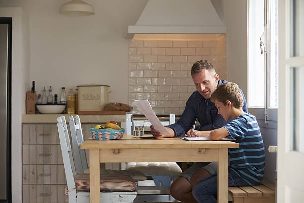 Father Helping Son With Homework Sitting At Kitchen Table Father Helping Son With Homework Sitting At Kitchen Table homework table stock pictures, royalty-free photos & images