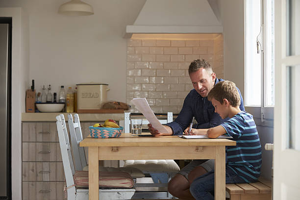 homework time images Father Helping Son With Homework Sitting At Kitchen Table Father Helping Son With Homework Sitting At Kitchen Table homework table stock pictures, royalty-free photos & images