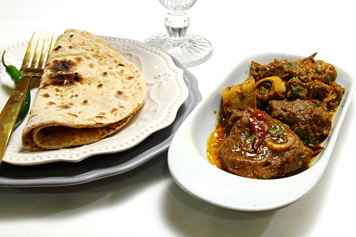 A bowl of mutton curry or Rogan josh and a plate of Chapati on white background