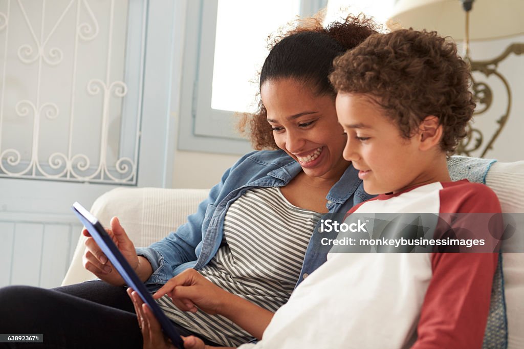 Mother And Son Sitting On Sofa Using Digital Tablet Mother Stock Photo