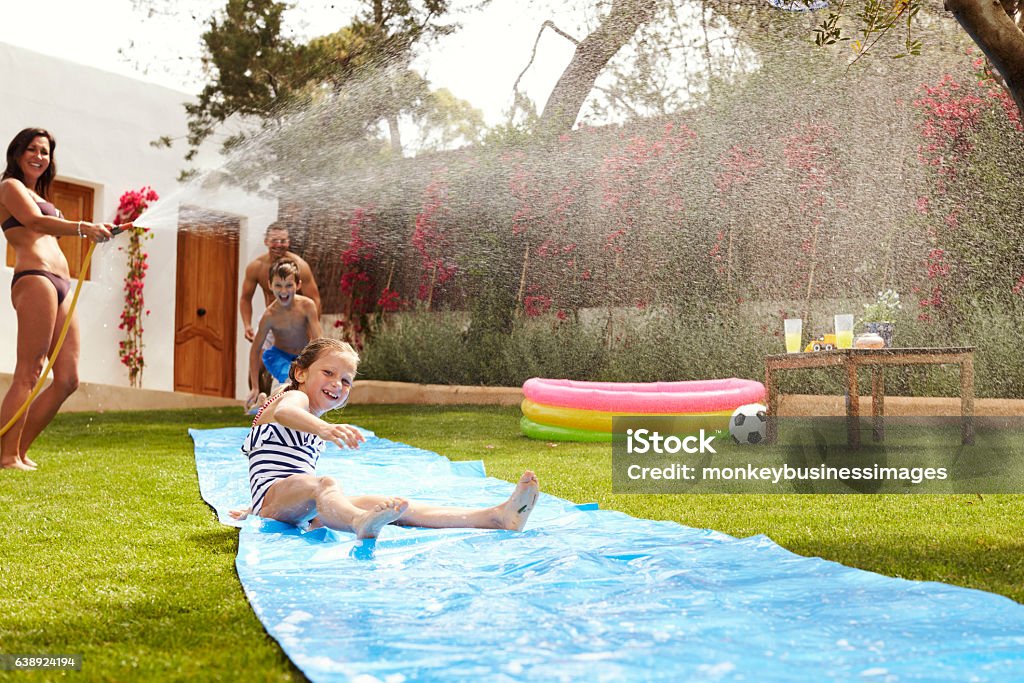 Family Having Fun On Water Slide In Garden Yard - Grounds Stock Photo