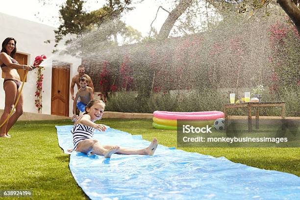 Family Having Fun On Water Slide In Garden Stock Photo - Download Image Now - Yard - Grounds, Summer, Water