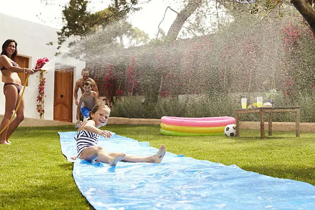 Photo of Family Having Fun On Water Slide In Garden