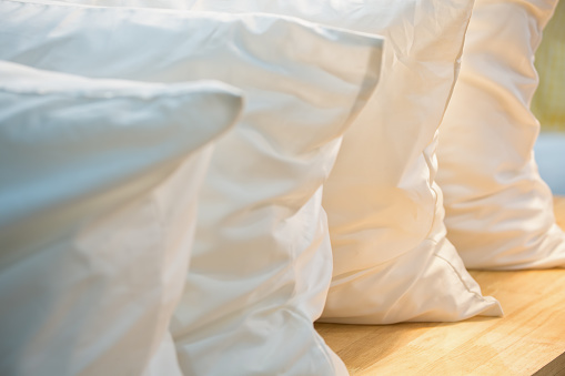 Row of white pillows with shallow depth of field on a wooden table arranged under sunlight.