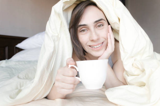 istock Pretty Woman Snuggled Under Duvet Drinking Coffee 638928320