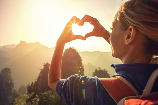 Young woman hiking in the Zhangjiajie National Forest park, makes a heart shape finger frame. Love nature wanderlust sharing concept.