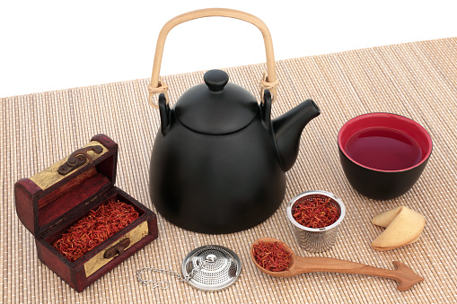 Safflower herbal tea with oriental teapot, cup, strainer, old wooden caddy and spoon with fortune cookie on bamboo over white background. Used also in chinese herbal medicine.