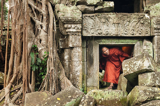 Monk exploring old ruins Cambodian monk ducks under a short doorway to explore an ancient temple with fallen stones and tangled roots encroaching the structure, Ta Prohm, Angkor Wat, Siem Reap, Cambodia, Asia angkor wat entrance stock pictures, royalty-free photos & images
