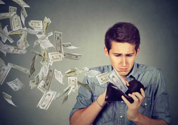 Photo of Man looking at wallet with money dollars flying away