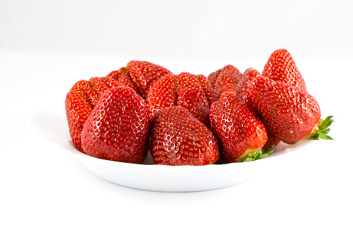 Ripe red strawberries in white plate on white background.