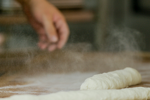 A hand flours the counter in an industrial kitchen in preparation for kneading dough.