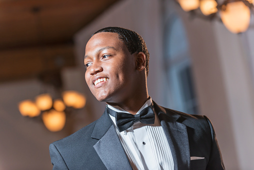 Young black Hispanic man wearing a tuxedo. He is smiling, dressed for a special event, perhaps a wedding or prom.