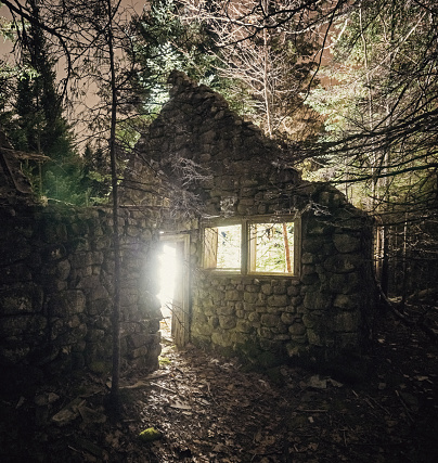 Light spills from a century old stone homestead dissapearing into the forest with time.  Long exposure.