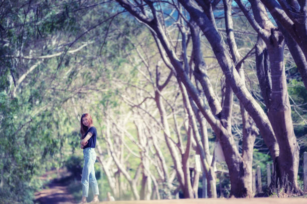 Beautiful asia woman in black t shirt and jeans stand on the road under tunnel tree in the sunny day,bright sunlight