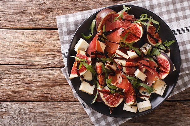Gourmet salad with figs, prosciutto, blue cheese and arugula Gourmet salad with figs, prosciutto, blue cheese and arugula close-up on a plate on the table. horizontal view from above plate fig blue cheese cheese stock pictures, royalty-free photos & images