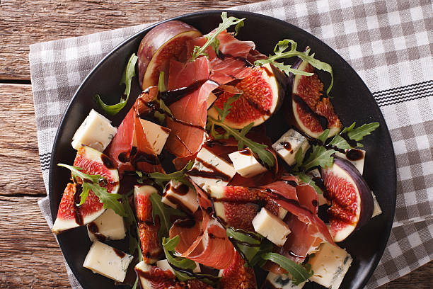 Salad with figs and Parma ham dressed with balsamic sauce Salad with figs, cheese, prosciutto and arugula dressed with balsamic sauce on a plate on the table. horizontal view from above plate fig blue cheese cheese stock pictures, royalty-free photos & images
