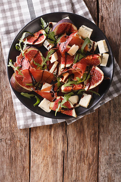 Gourmet salad with figs, prosciutto, blue cheese and arugula Gourmet salad with figs, prosciutto, blue cheese and arugula close-up on a plate on the table. vertical view from above plate fig blue cheese cheese stock pictures, royalty-free photos & images