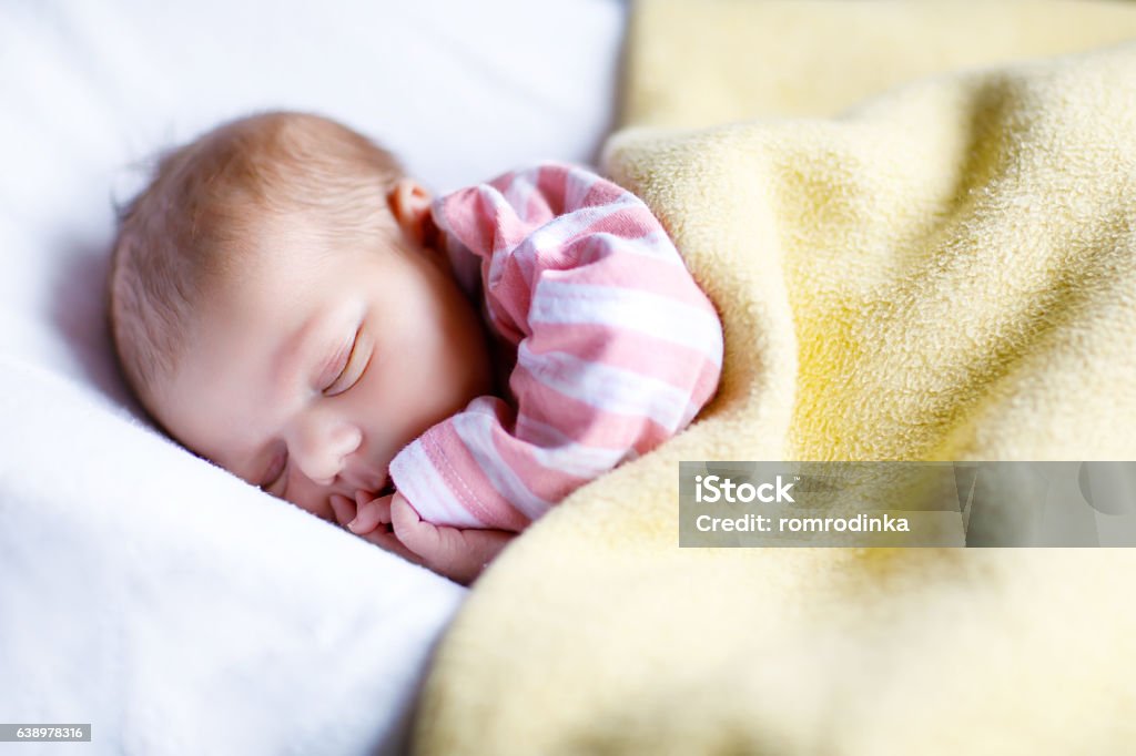 Portrait of cute adorable newborn baby girl sleeping Cute adorable newborn baby sleeping in white bed. New born child, little girl laying in bed. Family, new life, childhood, beginning concept. Girls Stock Photo
