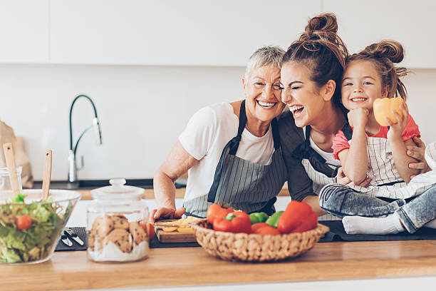 drei generationen frauen lachen in der küche - essen zubereiten fotos stock-fotos und bilder