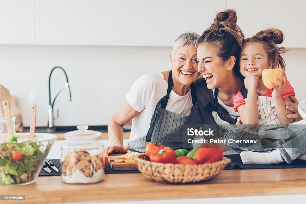 Três gerações de mulheres rindo na cozinha - Foto de stock de Família royalty-free Três gerações de mulheres rindo na cozinha - Foto de stock de Família royalty-free