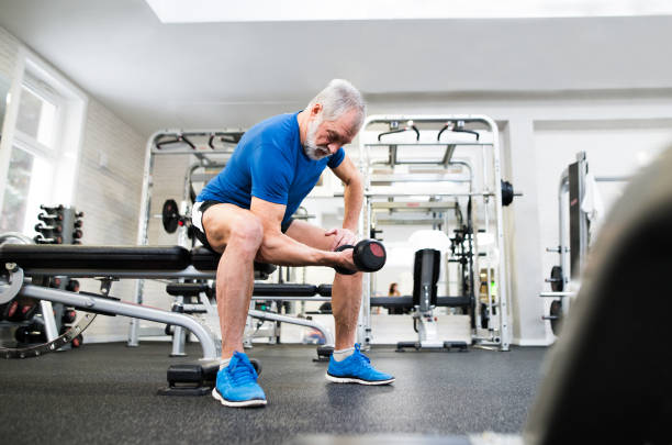 Senior man in gym working out with weights. Senior man in sports clothing in gym working out with weights. senior bodybuilders stock pictures, royalty-free photos & images