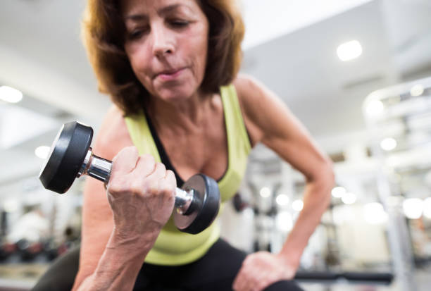 Senior woman in gym working out with weights. Senior woman in sports clothing in gym working out with weights. Close up of hands. senior bodybuilders stock pictures, royalty-free photos & images
