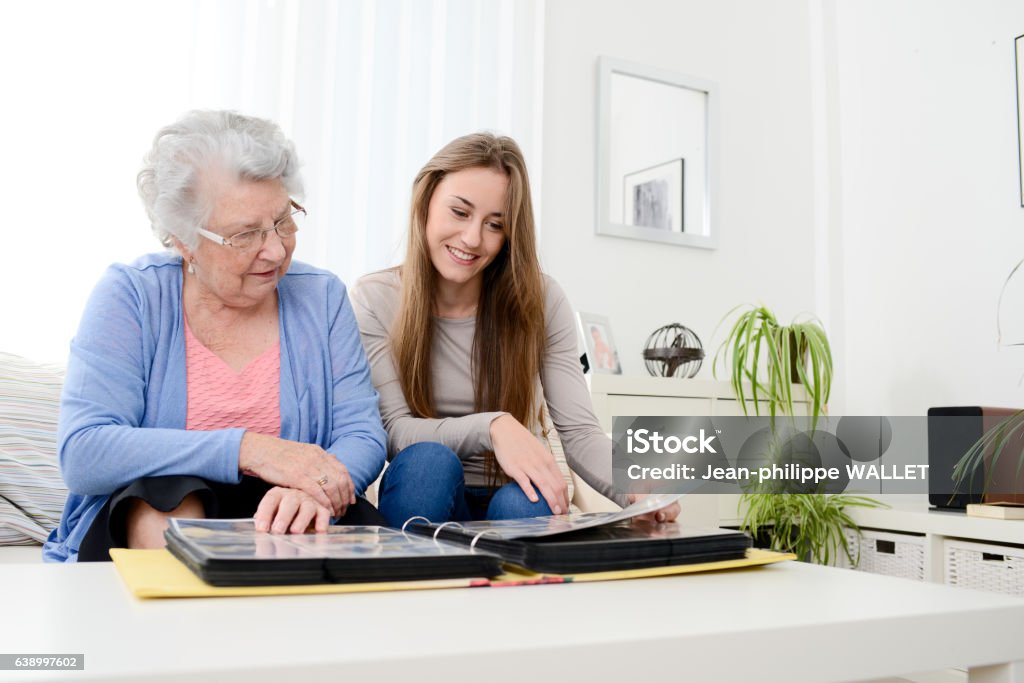 old senior woman with young granddaughter at home looking souvenir elderly woman with her young granddaughter at home looking at memory in family photo album Photo Album Stock Photo